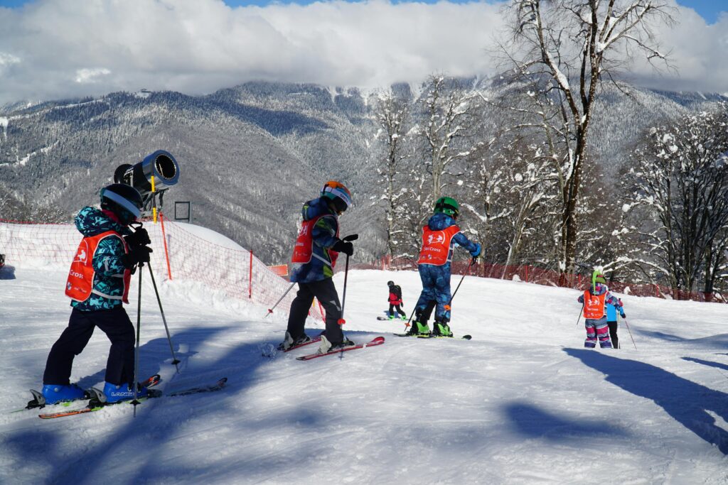 Group of children learning to ski on a snowy slope in Adlerskiy, Russia, under clear winter skies.
