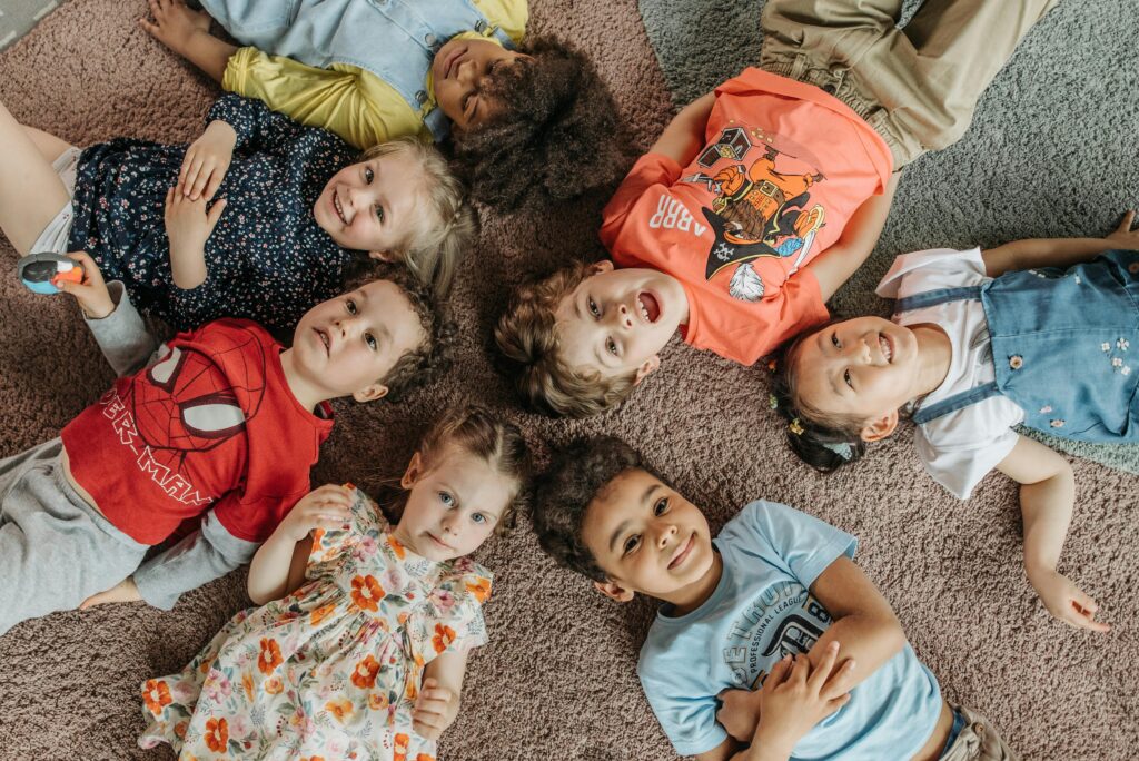 A joyful group of children lying on carpet, forming a circle and smiling at the camera.